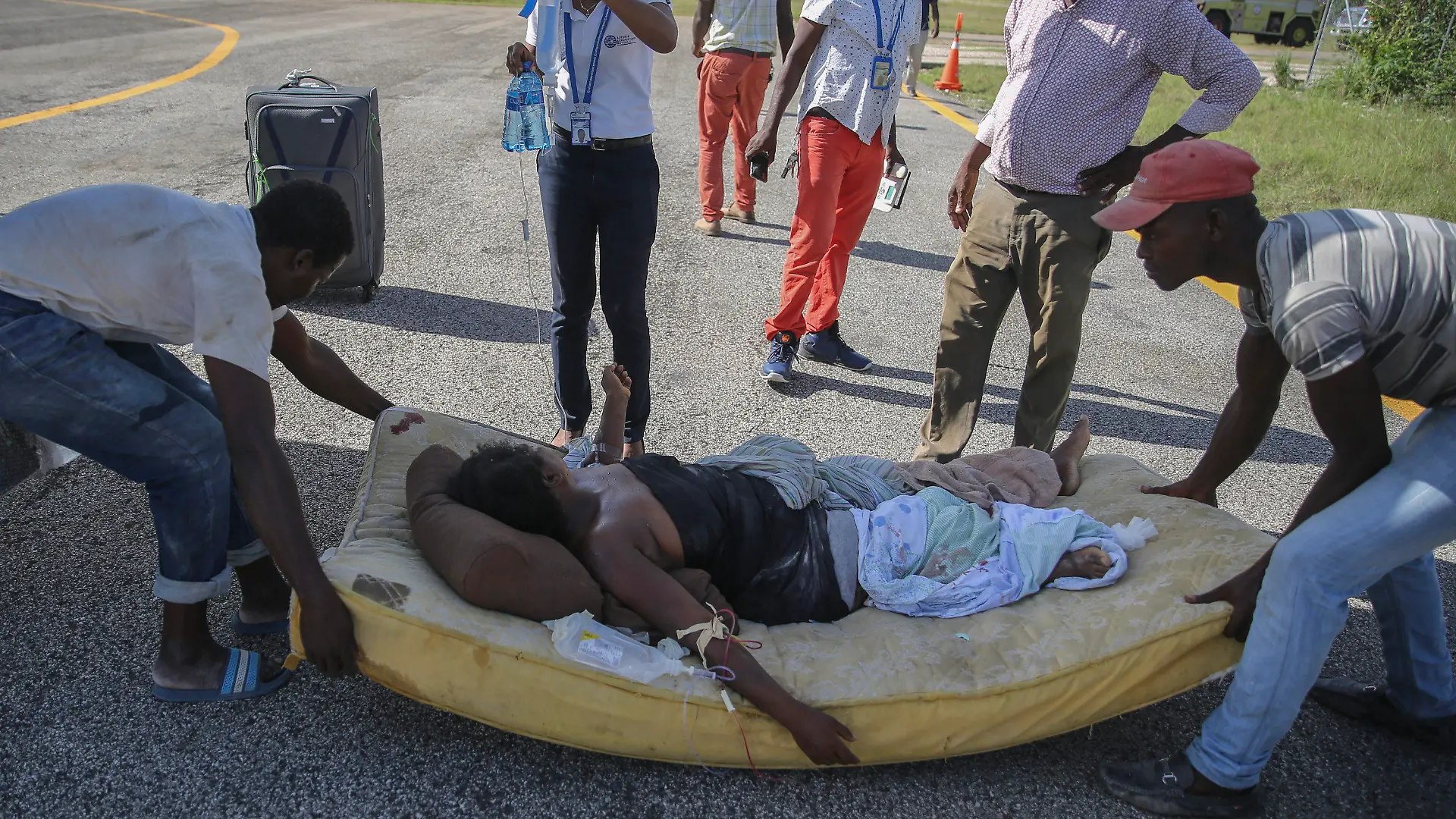 14.08.2021, Haiti, Les Cayes: Eine bei dem Erdbeben verletzte Frau wird in Les Cayes, Haiti, auf einer Matratze zu einem Flugzeug gebracht, das sie nach Port-au-Prince fliegt. Ein Erdbeben der Stärke 7,2 hat Haiti am Samstag erschüttert. Das Epizentrum lag etwa 125 Kilometer westlich der Hauptstadt Port-au-Prince, teilte der US Geological Survey mit. Foto: Joseph Odelyn/AP/dpa +++ dpa-Bildfunk +++