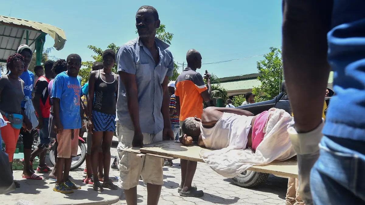 14.08.2021, Haiti, Les Cayes: Ein Mann hilft beim Tragen einer Person, die nach einem Erdbeben aus den Trümmern gerettet wurde. Ein schweres Erdbeben der Stärke 7,2 hat den Süden des Karibikstaates Haiti erschüttert. Dabei kamen mehrere Menschen ums Leben. Foto: Duples Plymouth/AP/dpa +++ dpa-Bildfunk +++