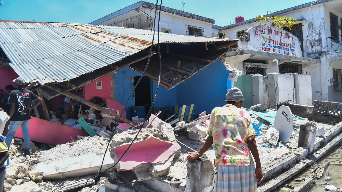 14.08.2021, Haiti, Les Cayes: Eine Frau steht vor einem zerstörten Haus nach einem Erdbeben in Les Cayes. Ein schweres Erdbeben der Stärke 7,2 hat den Süden des Karibikstaates Haiti erschüttert. Dabei kamen mehrere Menschen ums Leben. Foto: Duples Plymouth/AP/dpa +++ dpa-Bildfunk +++