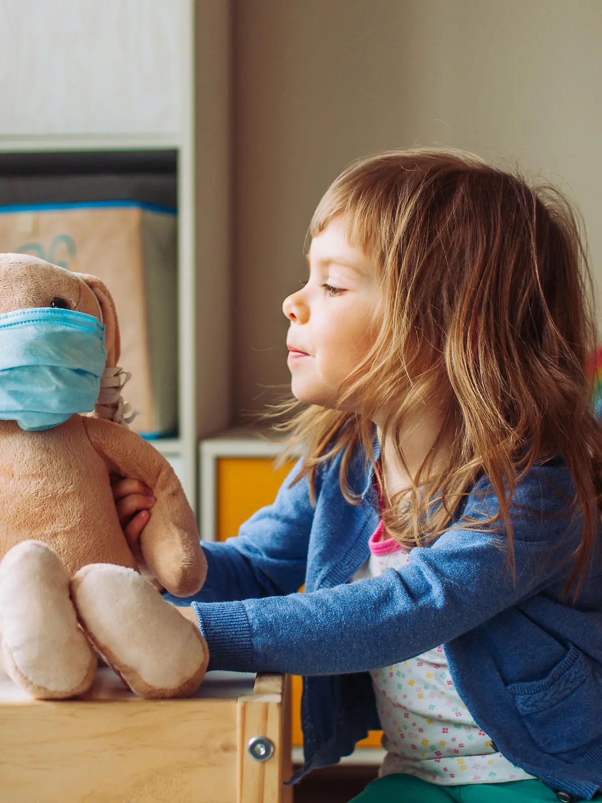 Ein kleines Mädchen hat ihrem Kuscheltier eine Mund-Nasenschutz-Maske aufgesetzt.