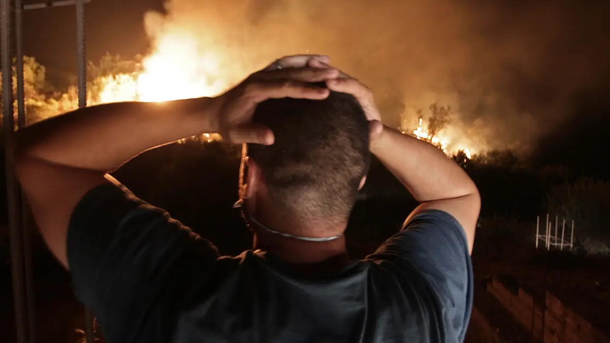 11.08.2021, Algerien, Larbaa Nath Irathen: Ein Mann schlägt die Hände über dem Kopf zusammen, während er auf die Flammen eines Waldbrandes in der Nähe des Dorfes Larbaa Nath Irathen beobachtet. Feuerwehrleute kämpften gegen eine Reihe von Waldbränden im Norden Algeriens, bei denen laut Innenminister Beldjoud mindestens sechs Menschen in der Bergregion Kabyle ums Leben kamen. Er machte Brandstifter dafür verantwortlich. Foto: Fateh Guidoum/AP/dpa +++ dpa-Bildfunk +++
