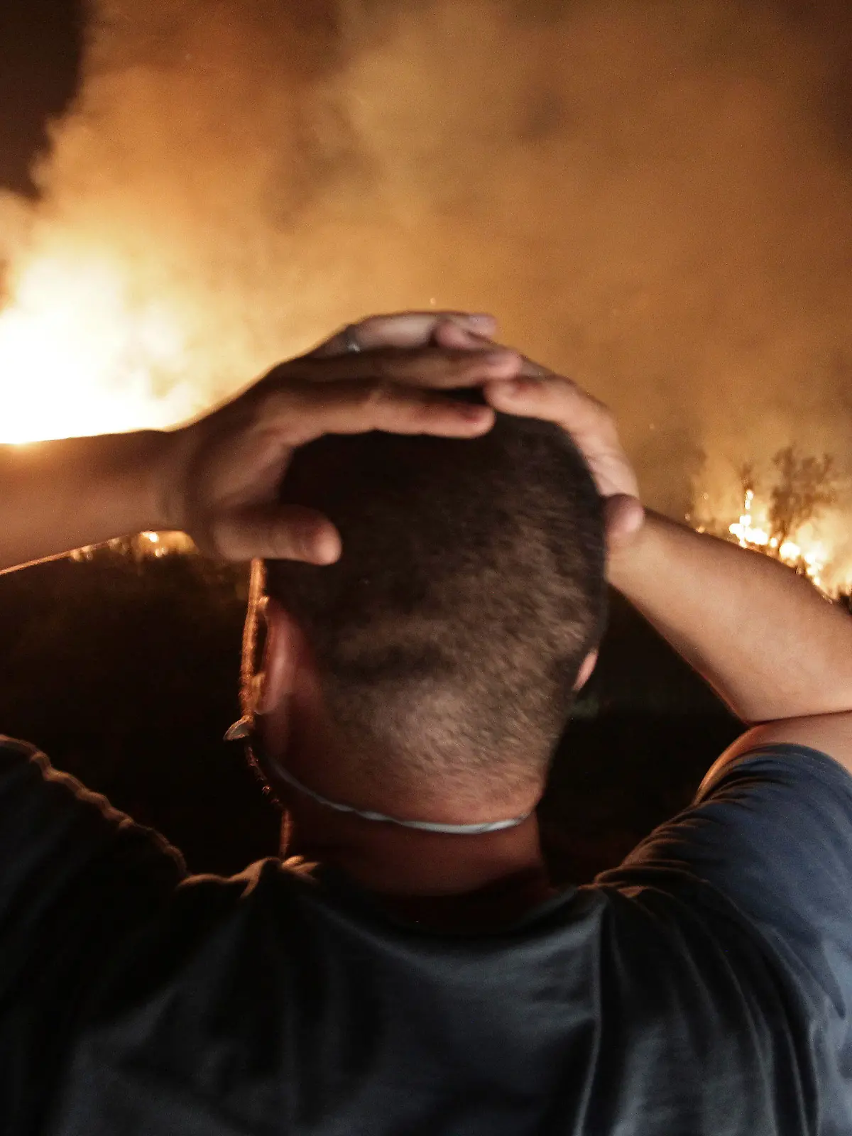 11.08.2021, Algerien, Larbaa Nath Irathen: Ein Mann schlägt die Hände über dem Kopf zusammen, während er auf die Flammen eines Waldbrandes in der Nähe des Dorfes Larbaa Nath Irathen beobachtet. Feuerwehrleute kämpften gegen eine Reihe von Waldbränden im Norden Algeriens, bei denen laut Innenminister Beldjoud mindestens sechs Menschen in der Bergregion Kabyle ums Leben kamen. Er machte Brandstifter dafür verantwortlich. Foto: Fateh Guidoum/AP/dpa +++ dpa-Bildfunk +++