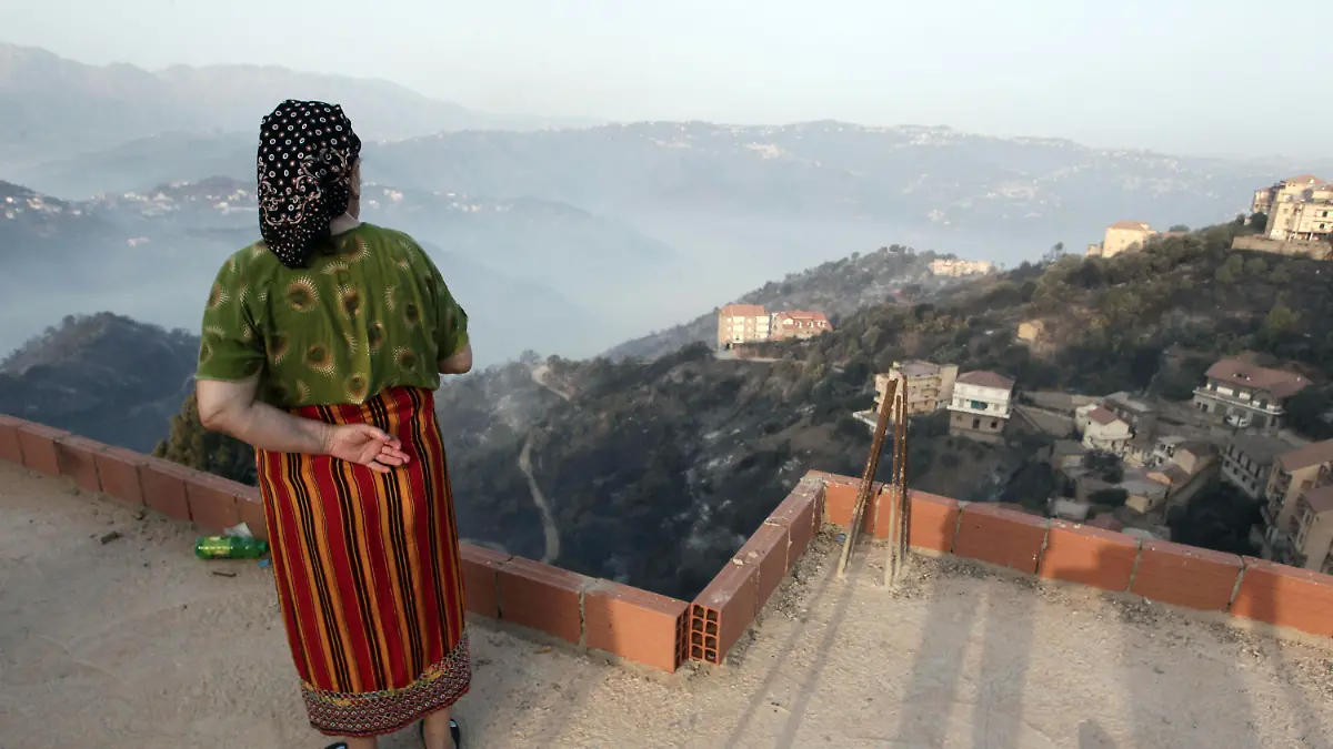 A woman looks at the landscape after wildfires in the village of Larbaa Nath Irathen, neat Tizi Ouzou, in the mountainous Kabyle region, 100 kilometers (60 miles) east of Algeria's capital of Algiers, Wednesday, Aug.11, 2021. At least 25 soldiers died saving residents from wildfires ravaging mountain forests and villages east of Algeria's capital, the president announced Tuesday night as the civilian toll rose to at least 17. (AP Photo/Fateh Guidoum)