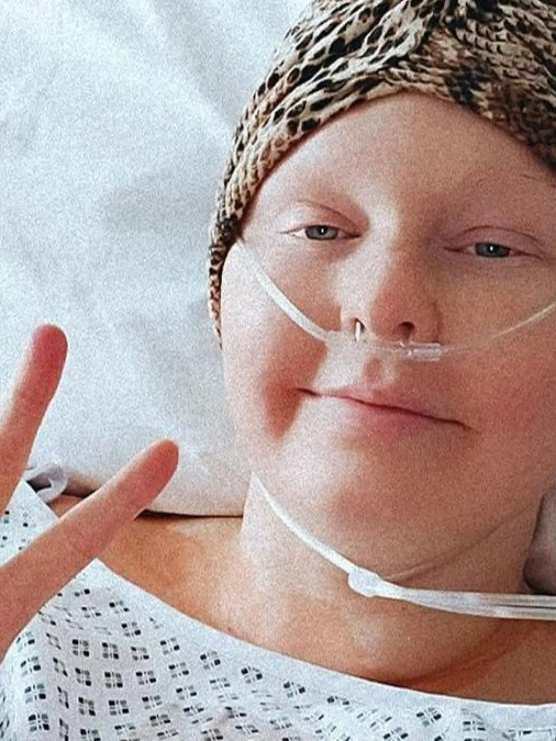 Eine junge Frau liegt während der Chemo-Therapie im Bett. Sie trägt eine Kopfbedeckung und man sieht Beatmungsschläuche.
