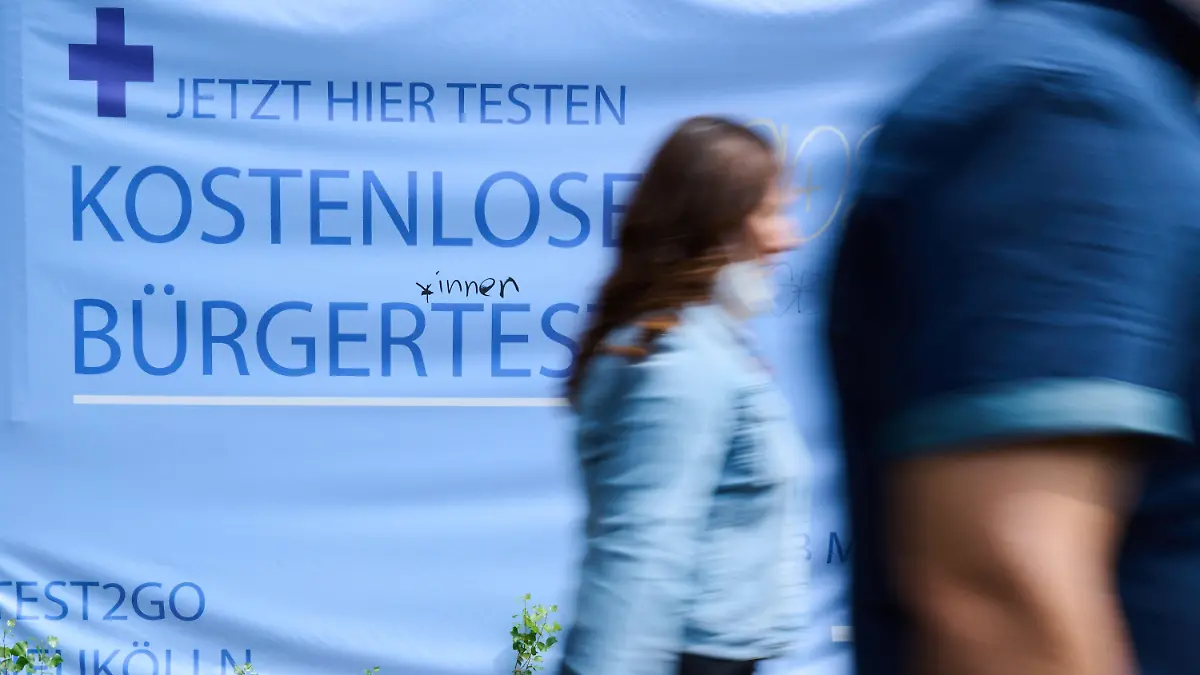 PRODUKTION - 09.08.2021, Berlin: «Kostenlose Bürgertests» steht auf einem Plakat während Personen vorüber gehen. Die Regierungschefs der Länder beraten am 10.08.2021 mit Bundeskanzlerin Merkel über den weiteren Umgang mit Corona-Impfungen und Tests. Foto: Annette Riedl/dpa +++ dpa-Bildfunk +++