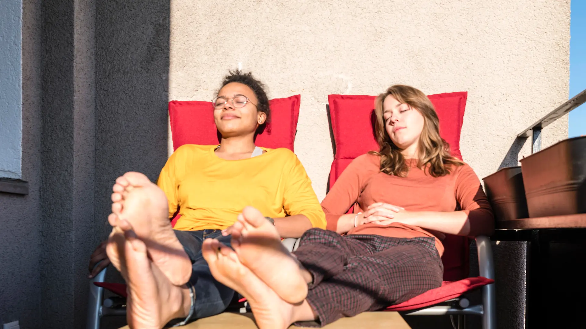 Zwei junge Frauen sitzen auf einem Balkon in der Sonne.