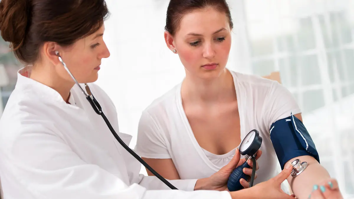 Female doctor checking young woman blood pressure