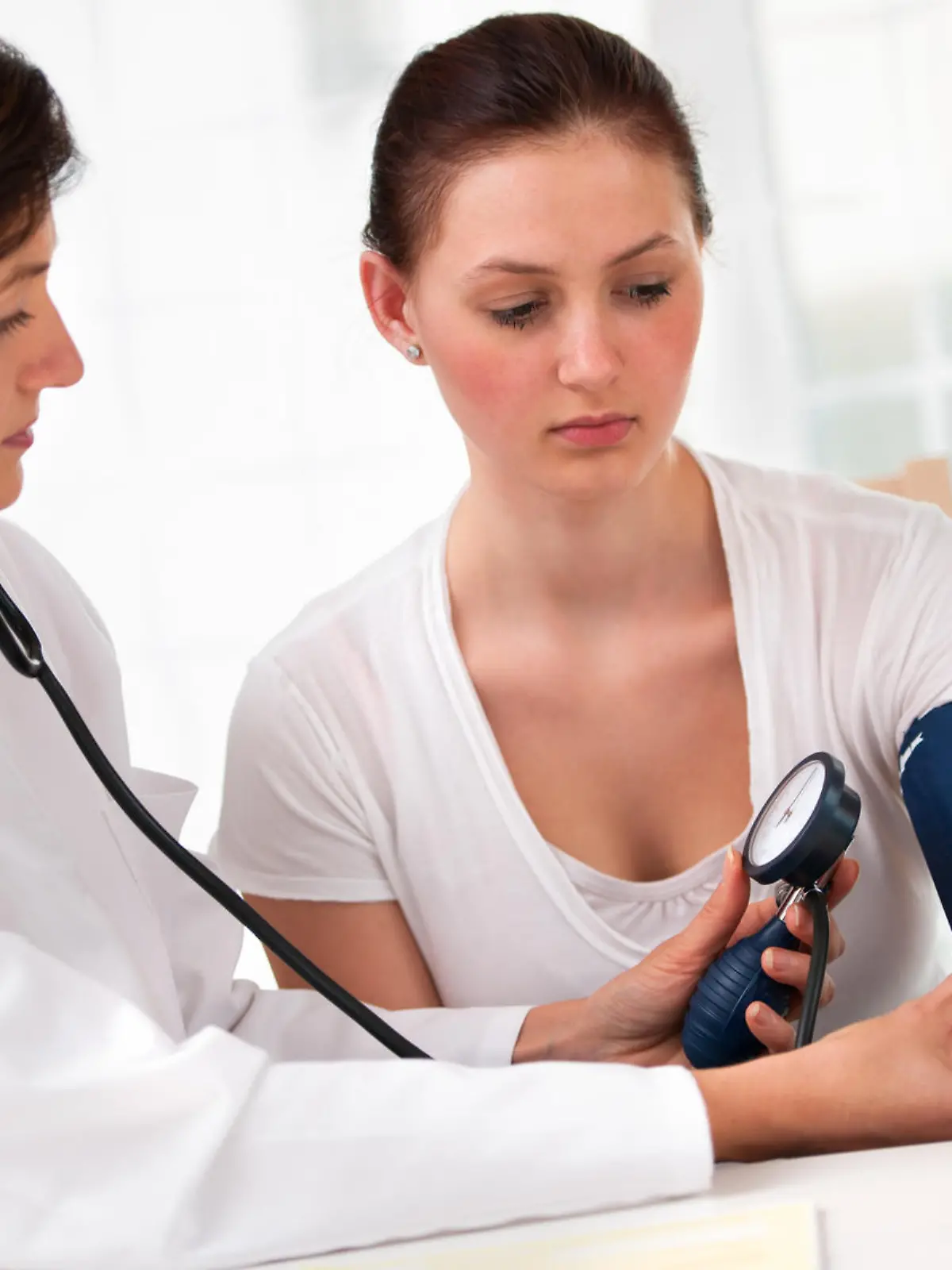 Female doctor checking young woman blood pressure