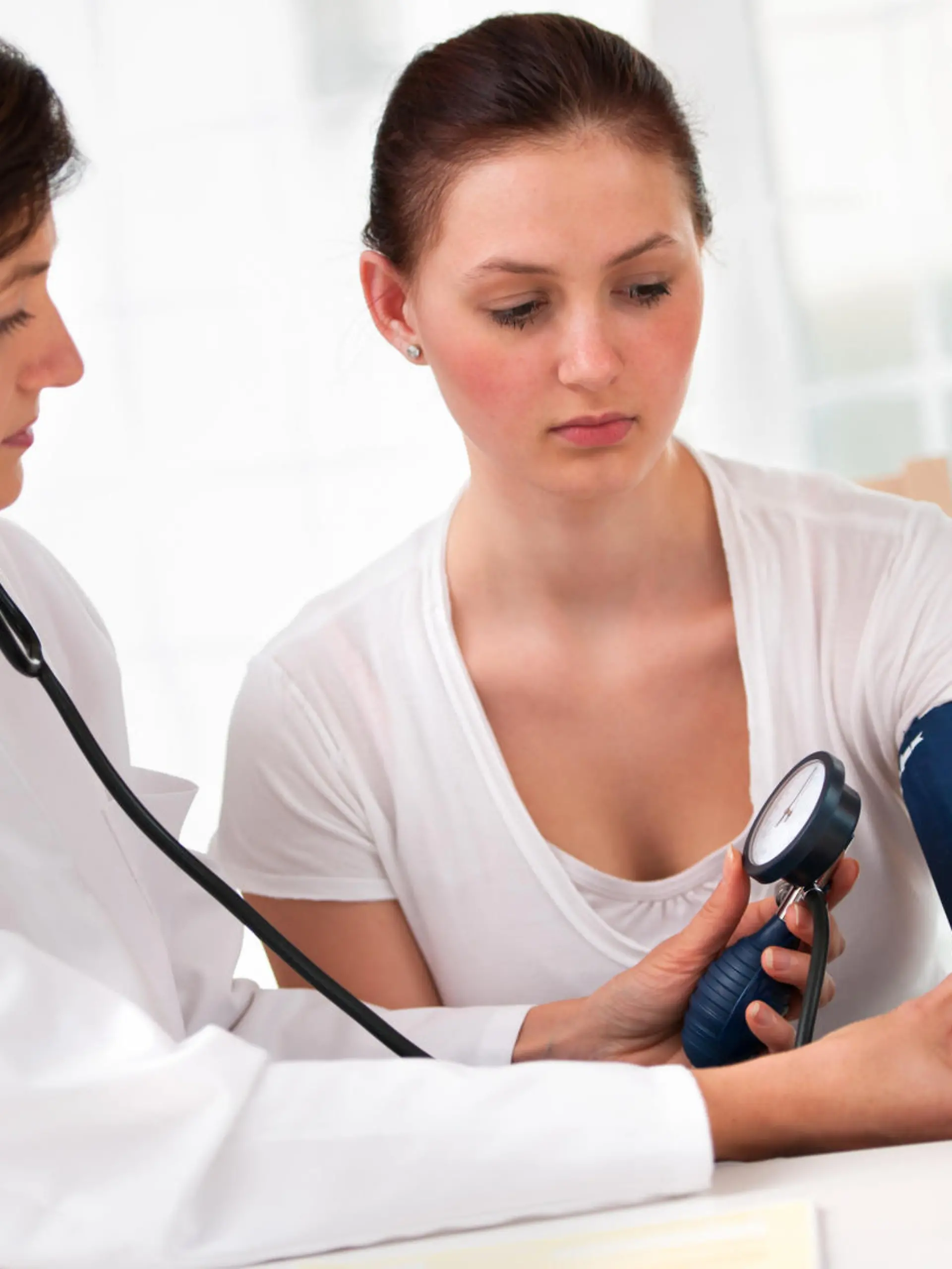 Female doctor checking young woman blood pressure