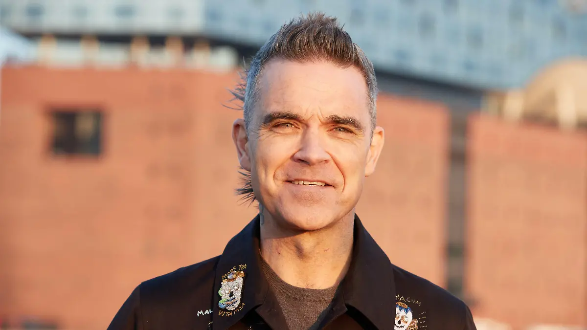 14.11.2022, Hamburg: Robbie Williams, britischer Sänger und Songwriter, steht während eines Fototermins auf einer Barkasse im Hamburger Hafen. Im Hintergrund ist die Elbphilharmonie zu sehen. Robbie Williams gibt am 15.11.2022 anlässlich der Feier seiner 25-jährigen Solo-Karriere ein Konzert in der Elbphilharmonie. Foto: Georg Wendt/dpa +++ dpa-Bildfunk +++