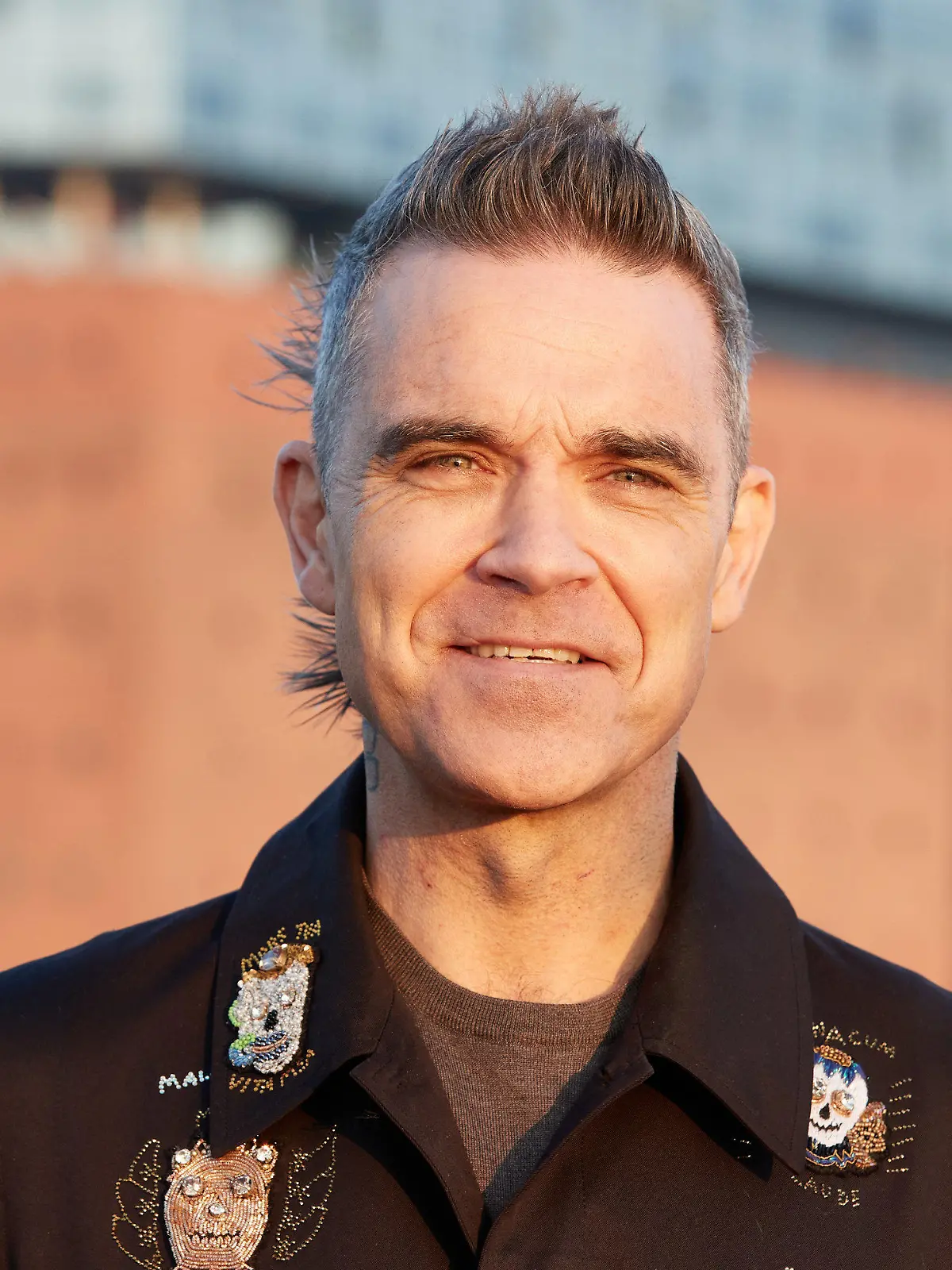 14.11.2022, Hamburg: Robbie Williams, britischer Sänger und Songwriter, steht während eines Fototermins auf einer Barkasse im Hamburger Hafen. Im Hintergrund ist die Elbphilharmonie zu sehen. Robbie Williams gibt am 15.11.2022 anlässlich der Feier seiner 25-jährigen Solo-Karriere ein Konzert in der Elbphilharmonie. Foto: Georg Wendt/dpa +++ dpa-Bildfunk +++