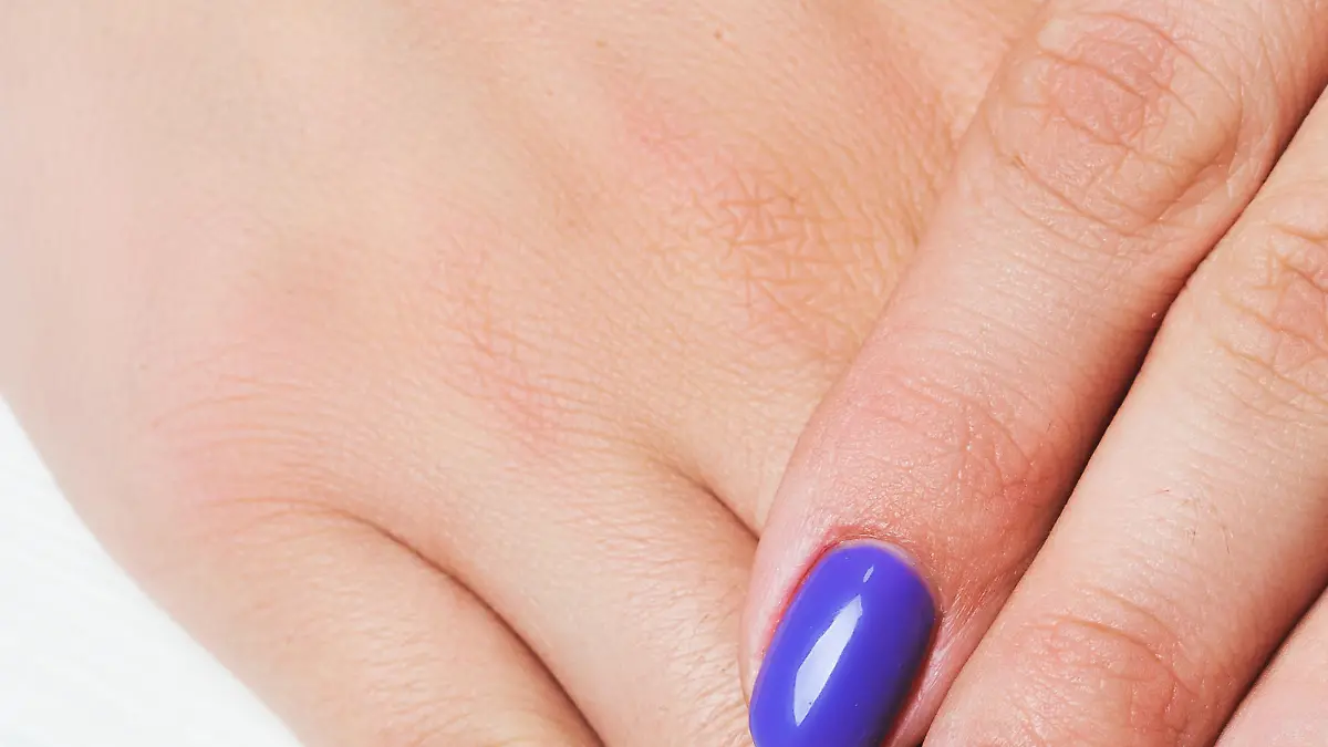 Purple nail art with pink floral pattern on white wooden backgroundPurple nail art with pink floral pattern on white wooden background