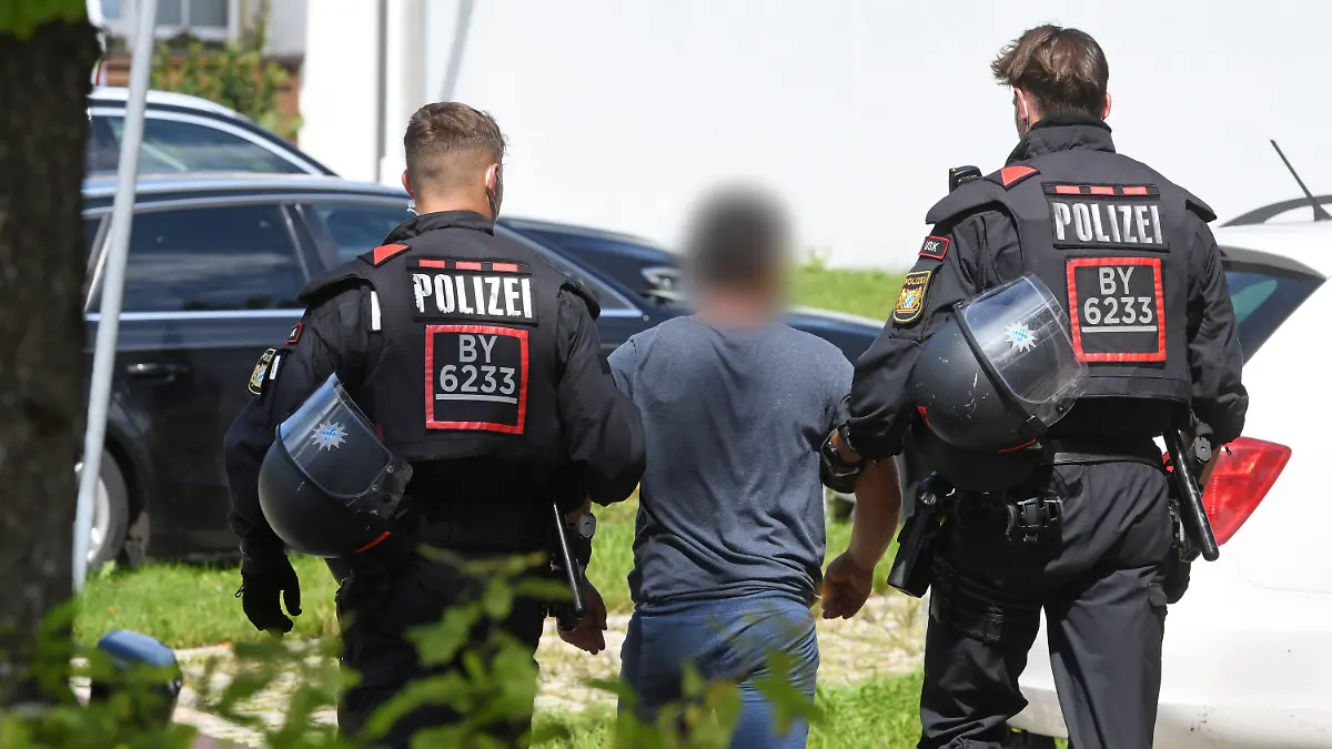 10.08.2021, Bayern, Miesbach: Zwei Einsatzkräfte der Polizei führen vor der Polizeiinspektion einen Tatverdächtigen ab. Mitglieder einer Großfamilie wollten sich Zugang zur Polizeistation verschaffen und griffen die Beamten mit Steinen an. Vorausgegangen war die Festnahme einer Person wegen Verdachts auf ein Sexualdelikt. Foto: Tobias Hase/dpa - ACHTUNG: Der Tatverdächtige wurde aus rechtlichen Gründen gepixelt +++ dpa-Bildfunk +++