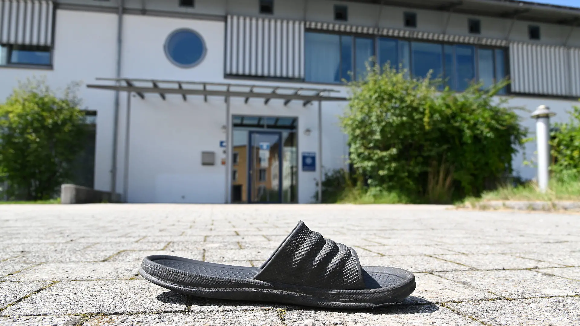 10.08.2021, Bayern, Miesbach: Eine Gummisandale liegt vor der Polizeiinspektion. Mitglieder einer Großfamilie wollten sich Zugang zur Polizeistation verschaffen und griffen die Beamten mit Steinen an. Vorausgegangen war die Festnahme einer Person wegen Verdachts auf ein Sexualdelikt. Foto: Tobias Hase/dpa +++ dpa-Bildfunk +++