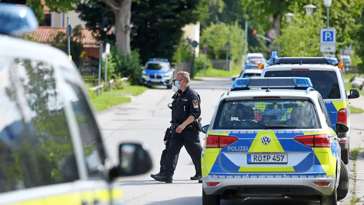 10.08.2021, Bayern, Miesbach: Zwei Einsatzkräfte der Polizei gehen vor der Polizeiinspektion zwischen Einsatzfahrzeugen vorbei. Mitglieder einer Großfamilie wollten sich Zugang zur Polizeistation verschaffen und griffen die Beamten mit Steinen an. Vorausgegangen war die Festnahme einer Person wegen Verdachts auf ein Sexualdelikt. Foto: Tobias Hase/dpa +++ dpa-Bildfunk +++