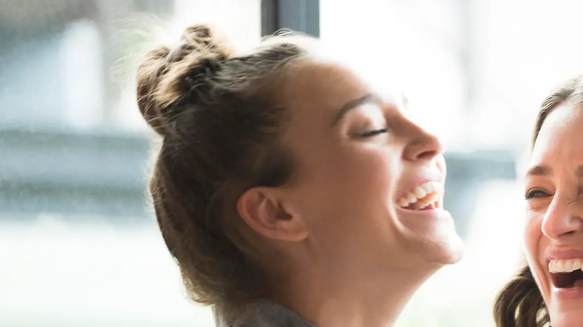 Two female friends with smartphone, smiling. Young woman holding phone, mid adult woman looking at her and laughing