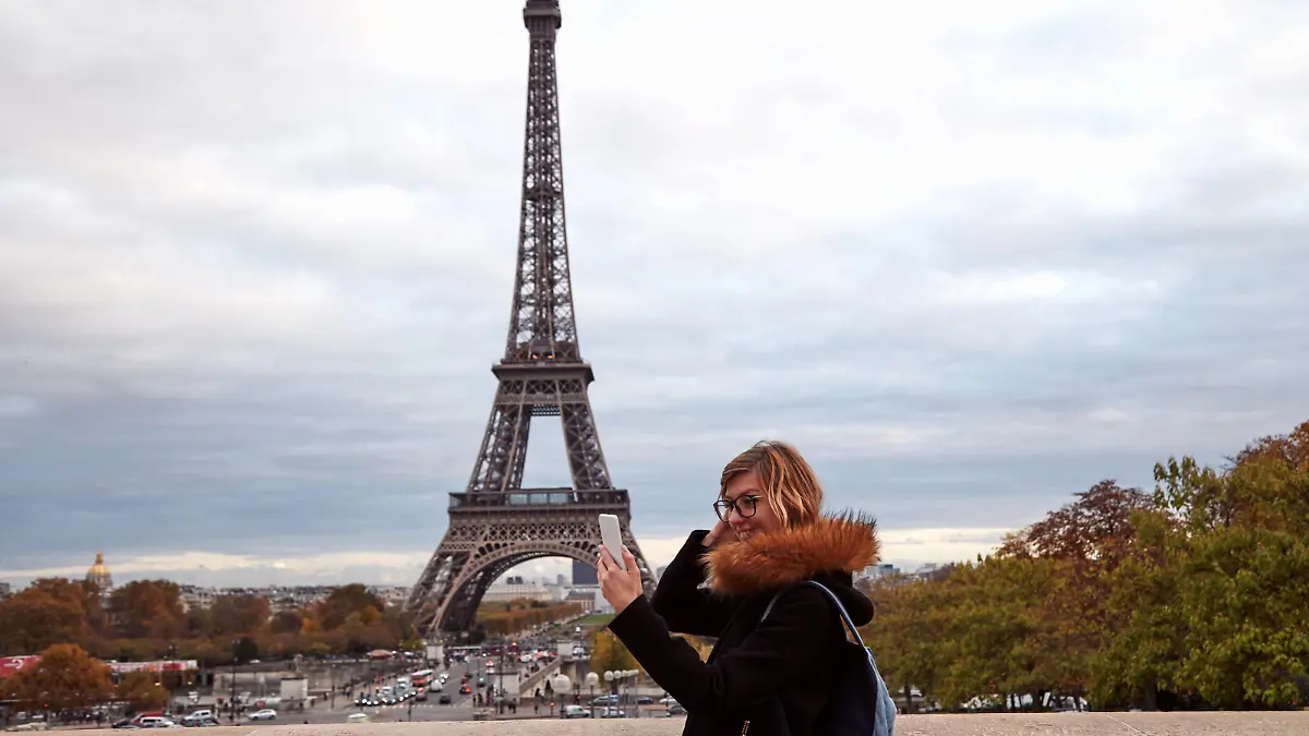 Eine junge Frau steht vor dem Eiffelturm und schaut auf ihr Handy.