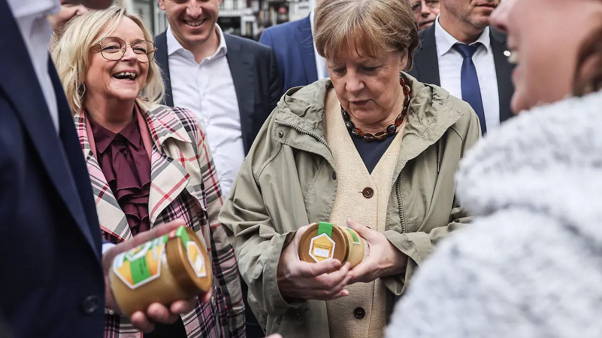 16.05.2023, Nordrhein-Westfalen, Bad Münstereifel: Die ehemalige Bundeskanzlerin Angela Merkel (Mr, CDU), bekommt beim Rundgang in Bad Münstereifel mit Bürgermeisterin Sabine Preiser-Marian (2.v.r., CDU) und Hendrik Wüst (r, CDU), Ministerpräsident Nordrhein-Westfalen von einer Anwohnerin Honig überreicht. Merkel und Wüst haben vor der Verleihung des Staatspreis an Merkel das von der Flutkatastrophe im Jahr 2021 stark betroffene Bad Münstereifel besucht. Damit löste Merkel ihr Versprechen aus dem Jahr 2021 ein, noch einmal wieder zu kommen. Foto: Oliver Berg/dpa +++ dpa-Bildfunk +++