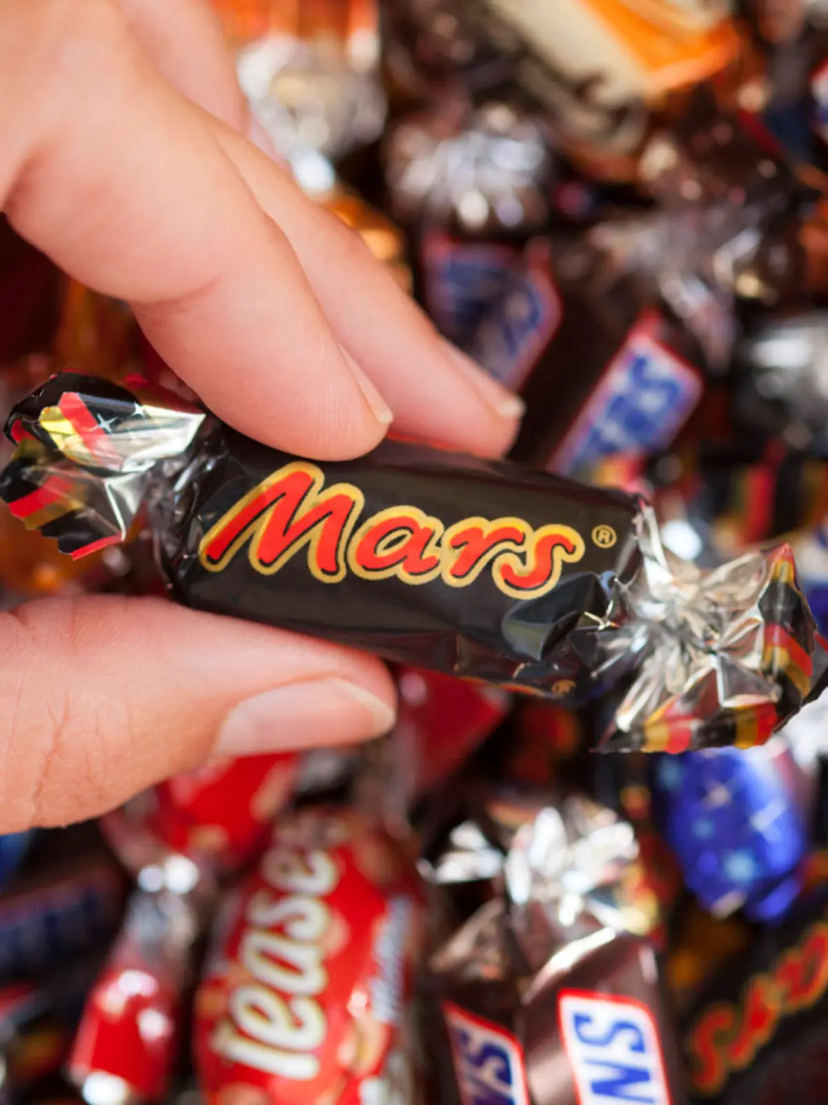 Paphos, Cyprus - December 19, 2013 Mars candy in woman's hand with background of Snickers, Mars, Twix, Milky Way, Galaxy, Bounty and Maltesers Teasers candies. Studio shot. All these candies manufactured by Mars, Incorporated.