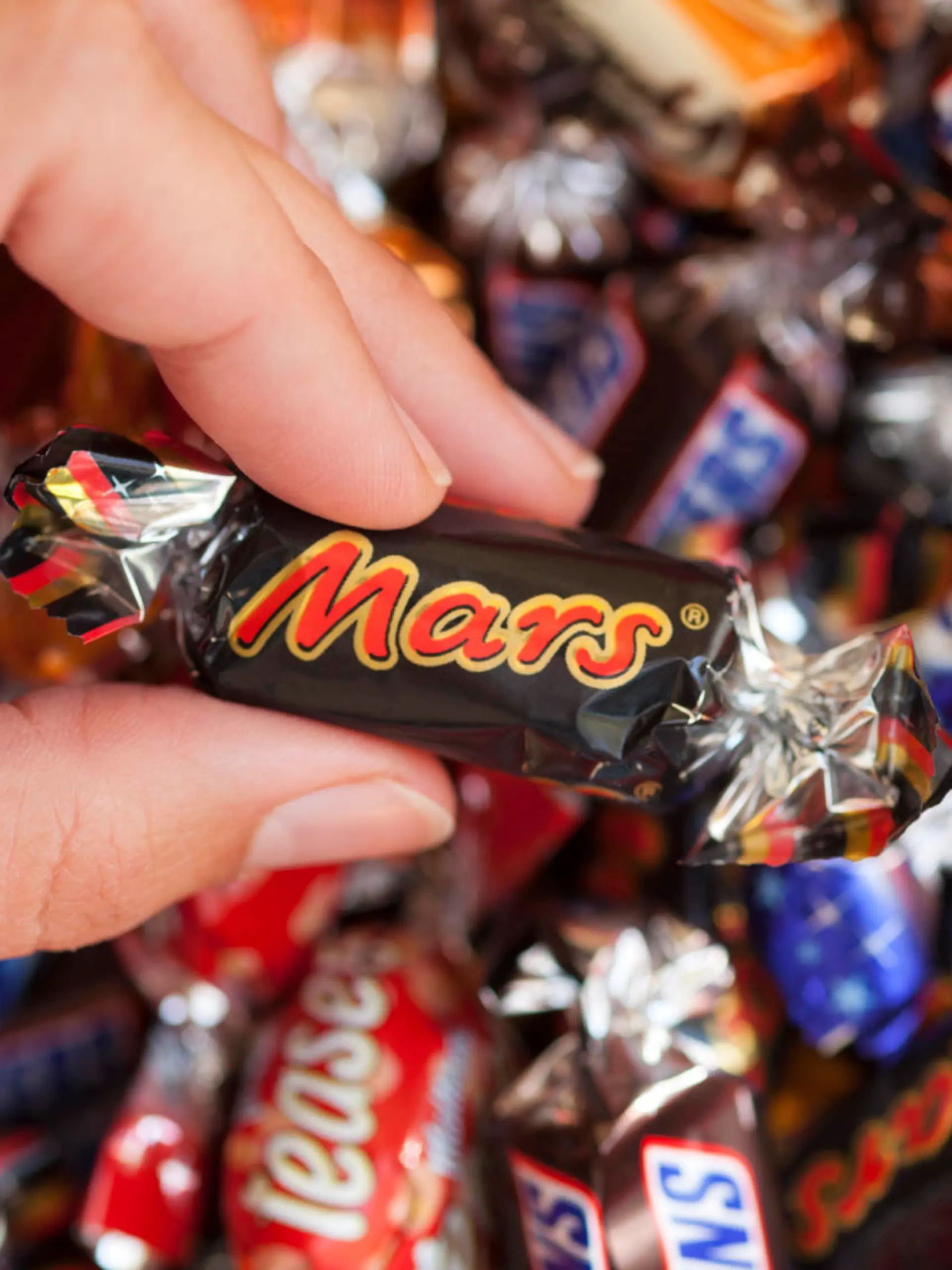 Paphos, Cyprus - December 19, 2013 Mars candy in woman's hand with background of Snickers, Mars, Twix, Milky Way, Galaxy, Bounty and Maltesers Teasers candies. Studio shot. All these candies manufactured by Mars, Incorporated.
