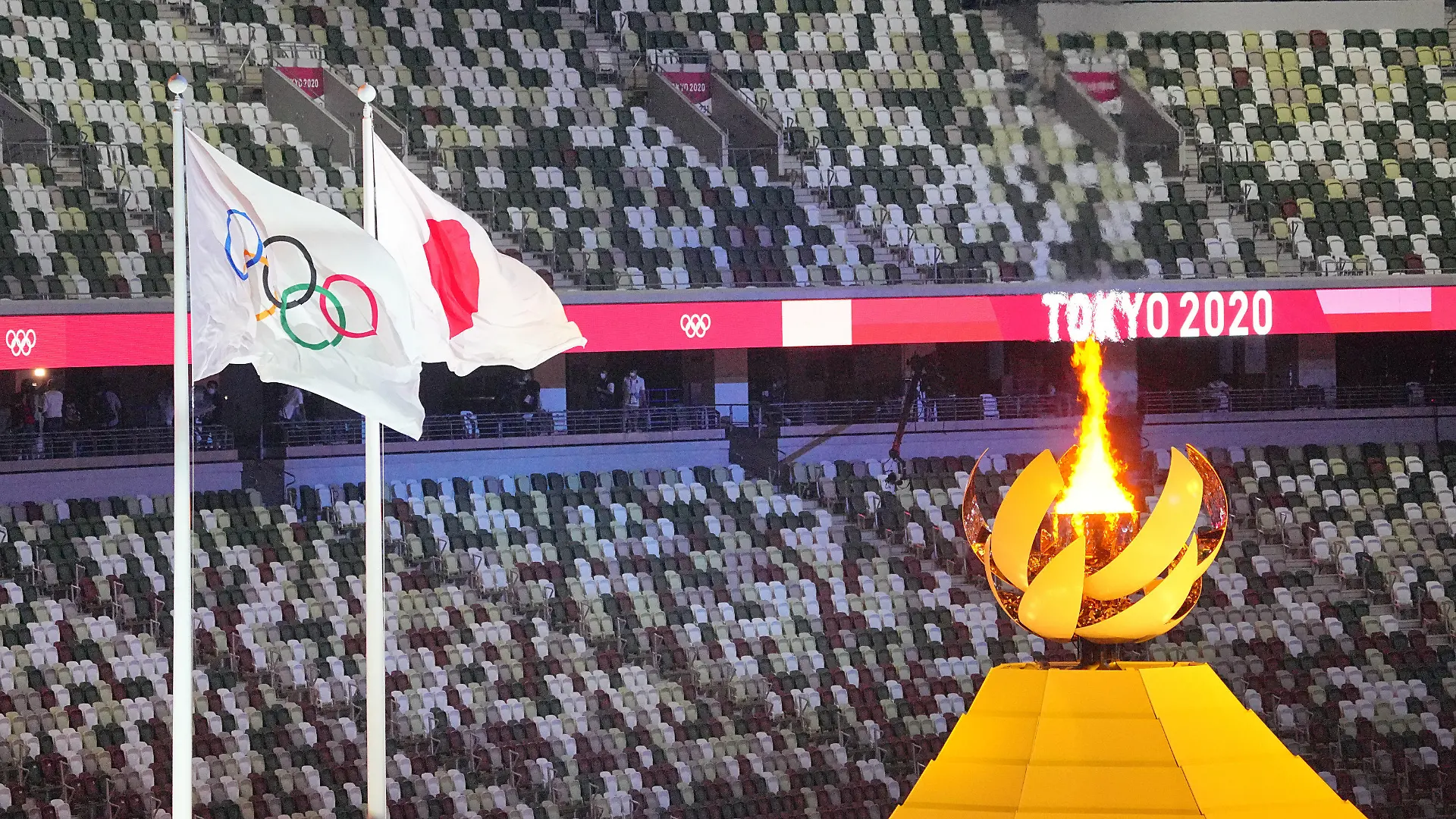 dpatopbilder - 23.07.2021, Japan, Tokio: Olympia: Eröffnungsfeier im Olympiastadion. Das Olympische Feuer brennt daneben die olympische und japanische Flagge. Foto: Michael Kappeler/dpa +++ dpa-Bildfunk +++