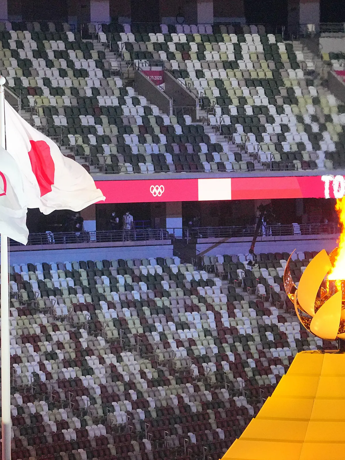 dpatopbilder - 23.07.2021, Japan, Tokio: Olympia: Eröffnungsfeier im Olympiastadion. Das Olympische Feuer brennt daneben die olympische und japanische Flagge. Foto: Michael Kappeler/dpa +++ dpa-Bildfunk +++