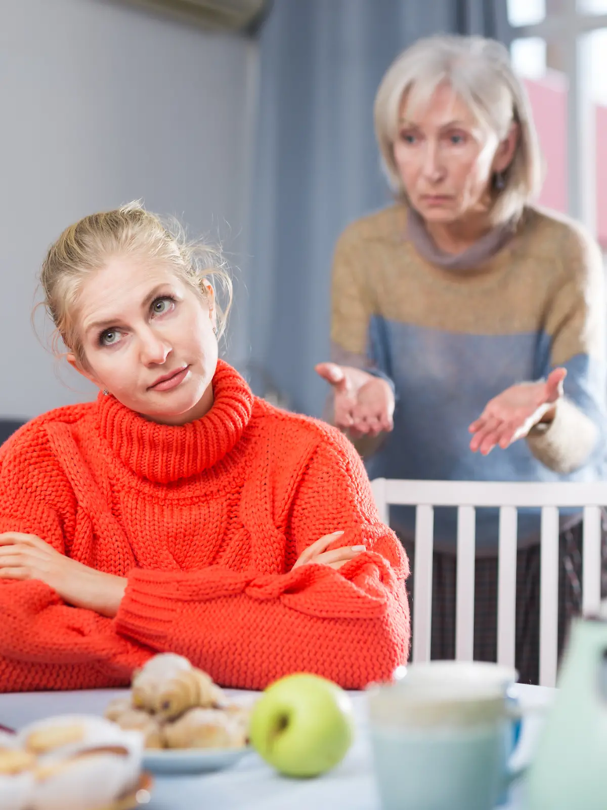 Erwachsene, aber junge Frau sitzt am gedeckten Küchentisch zu Weihnachten und muss sich von ihrer Mutter nervige Fragen zum Single-Dasein anhören
