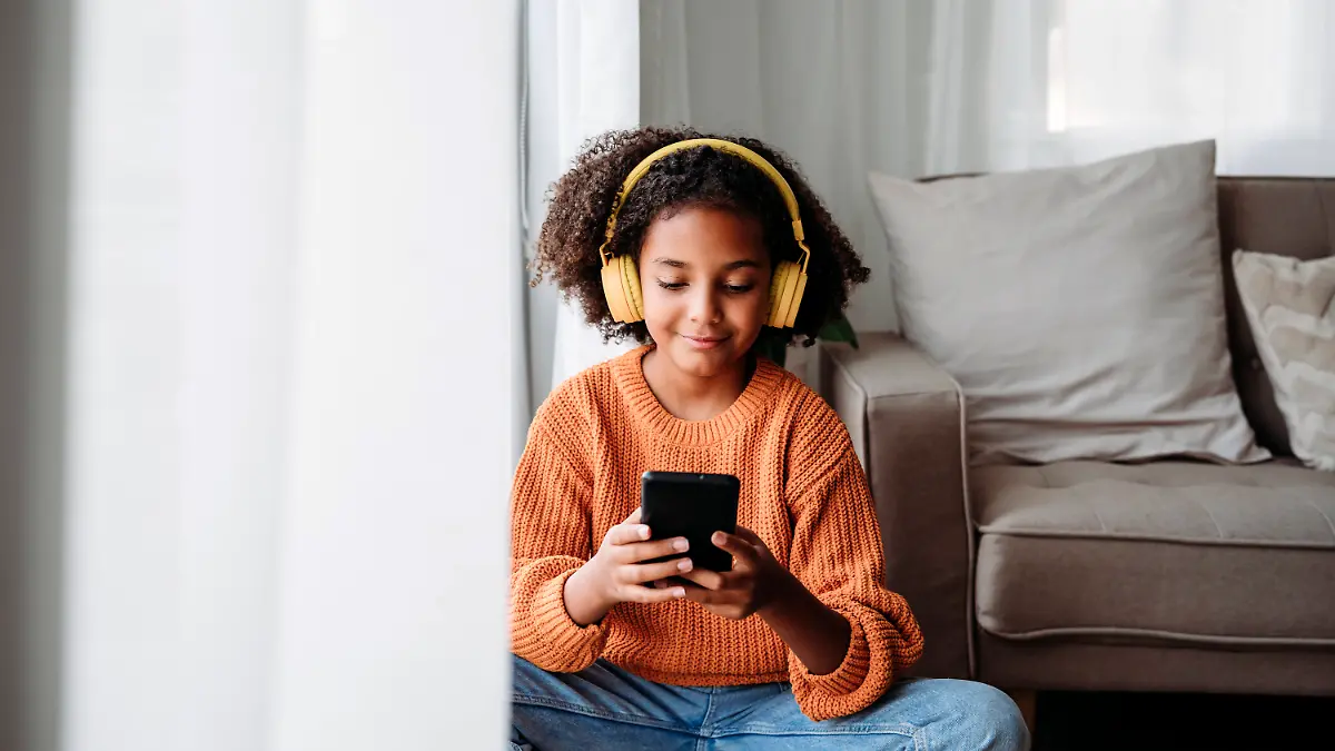 Ein Mädchen mit Kopfhörern schaut auf sein Smartphone und lächelt.