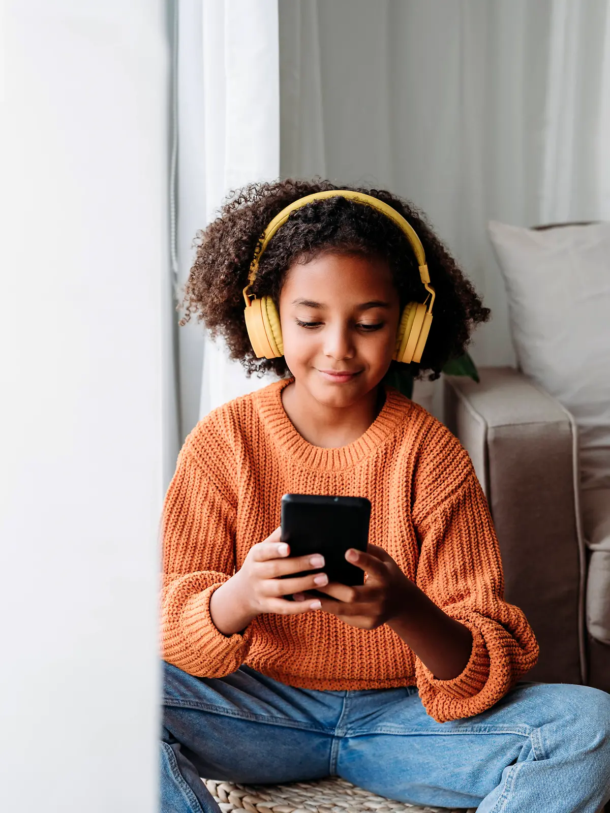 Ein Mädchen mit Kopfhörern schaut auf sein Smartphone und lächelt.