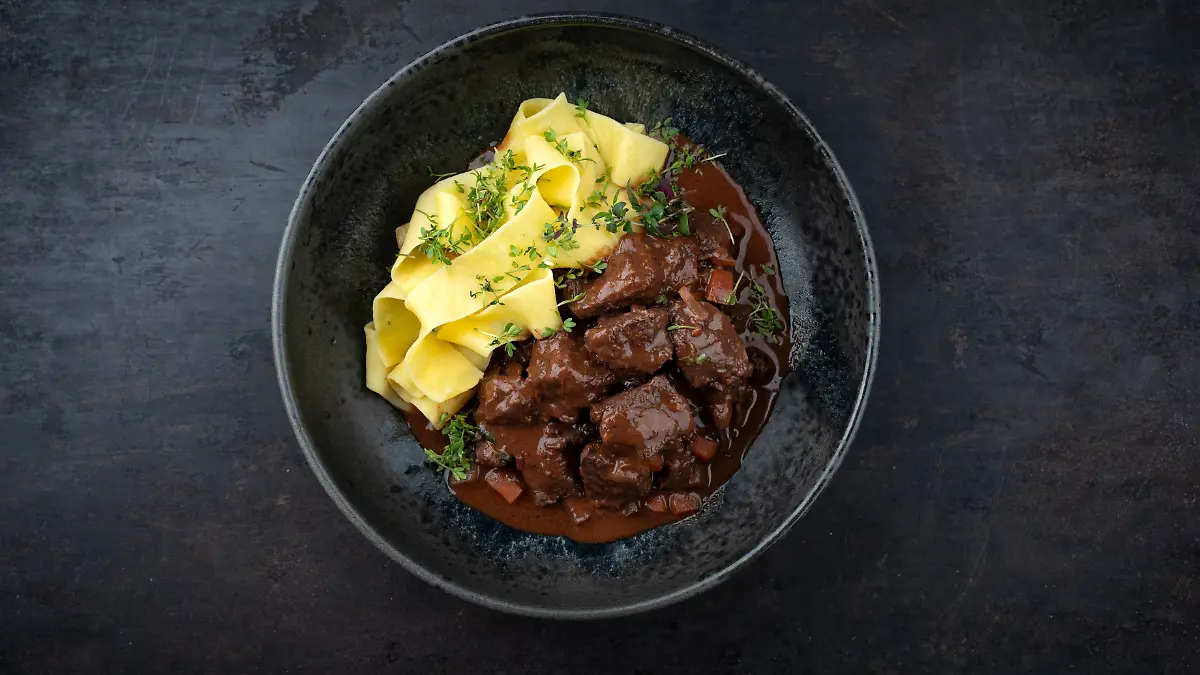 Traditionelles deutsches geschmortes Hirschragout mit Gemüse und Tagliatelle Pasta in süß würziger Schokoladen Rotweinsoße serviert als Draufsicht in einer Nordic Design Schale mit Textfreiraum