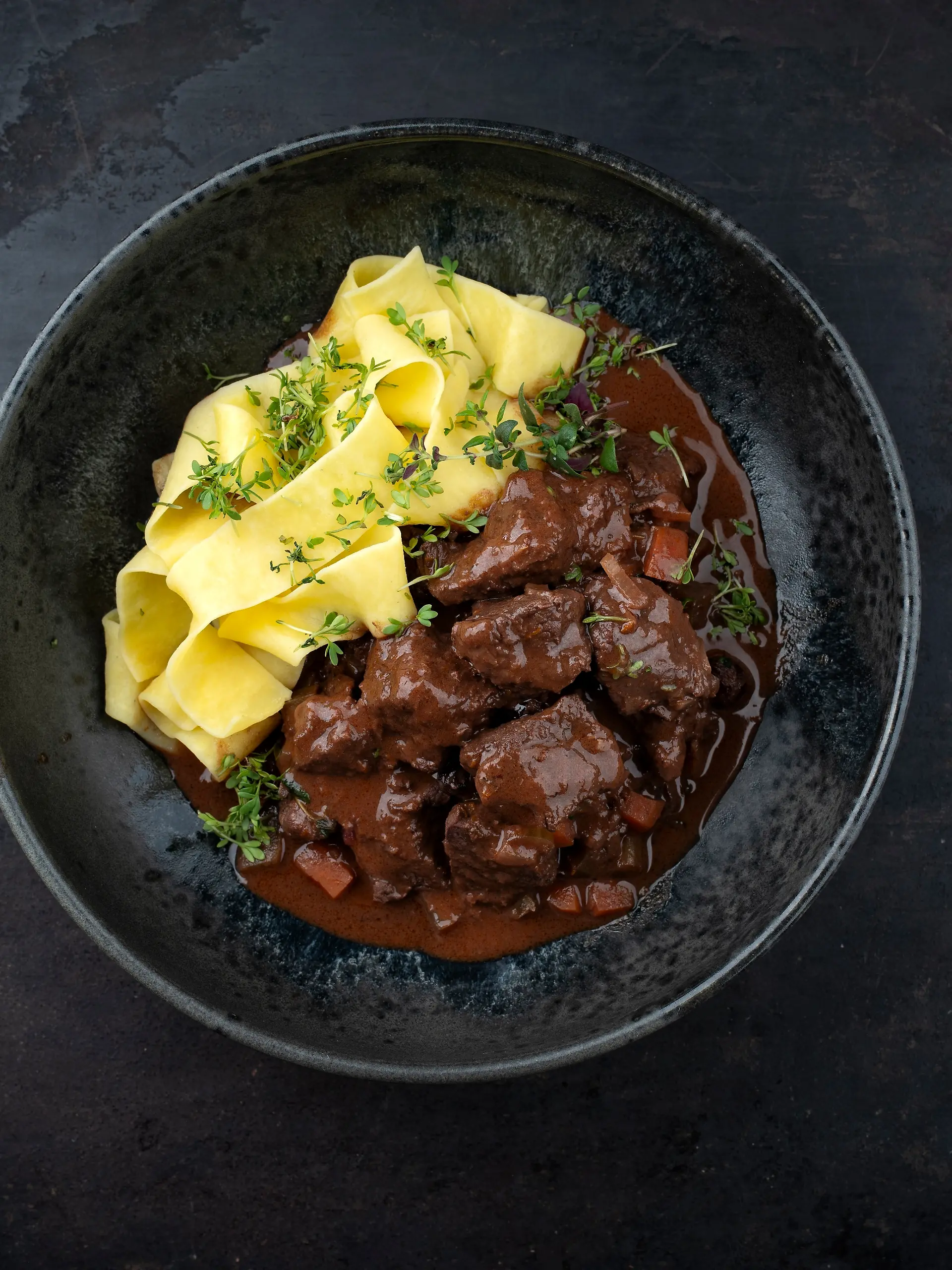 Traditionelles deutsches geschmortes Hirschragout mit Gemüse und Tagliatelle Pasta in süß würziger Schokoladen Rotweinsoße serviert als Draufsicht in einer Nordic Design Schale mit Textfreiraum