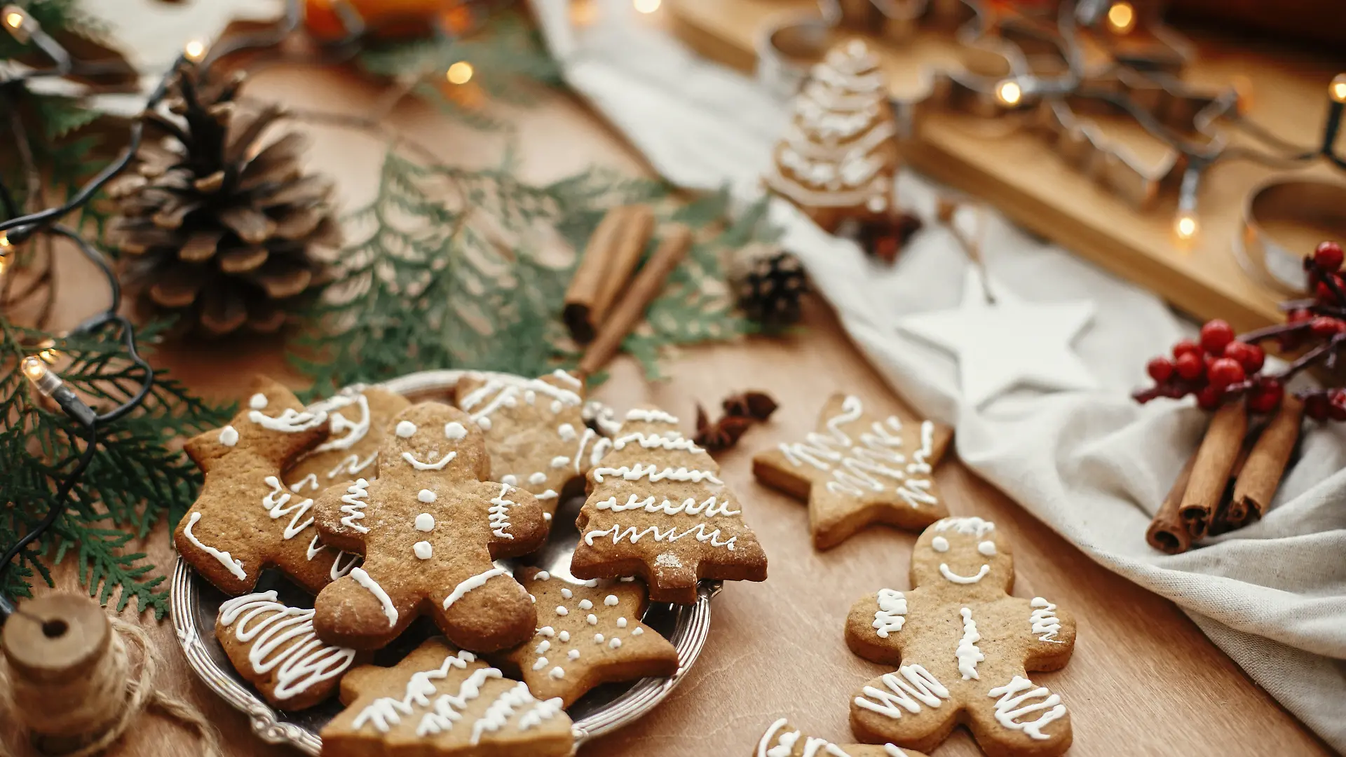 Weihnachts-Lebkuchenplätzchen auf einem Vintage-Teller und Anis, Zimt, Tannenzapfen, Zedernzweige mit goldenen Lichtern auf einem rustikalen Tisch.