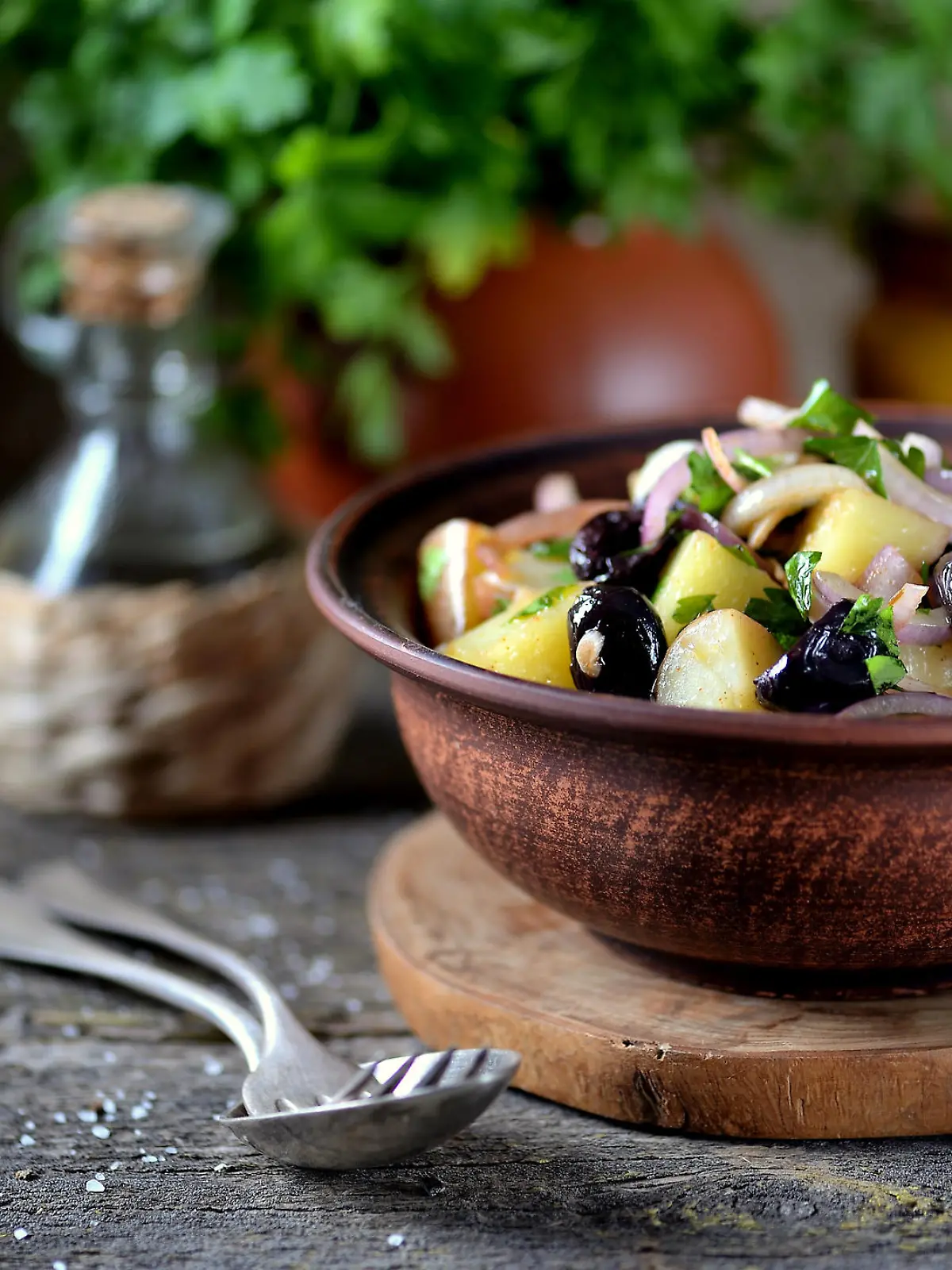 Kartoffelsalat mit Oliven und Zwiebeln in einer braunen Schüssel angerichtet