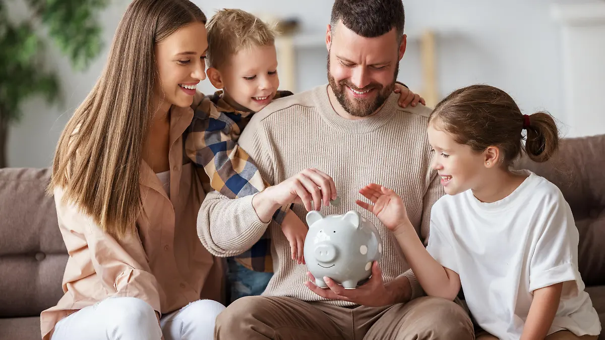 Happy family: cheerful mother and father with kids smiling and putting coins into piggy bank while sitting on sofa at home