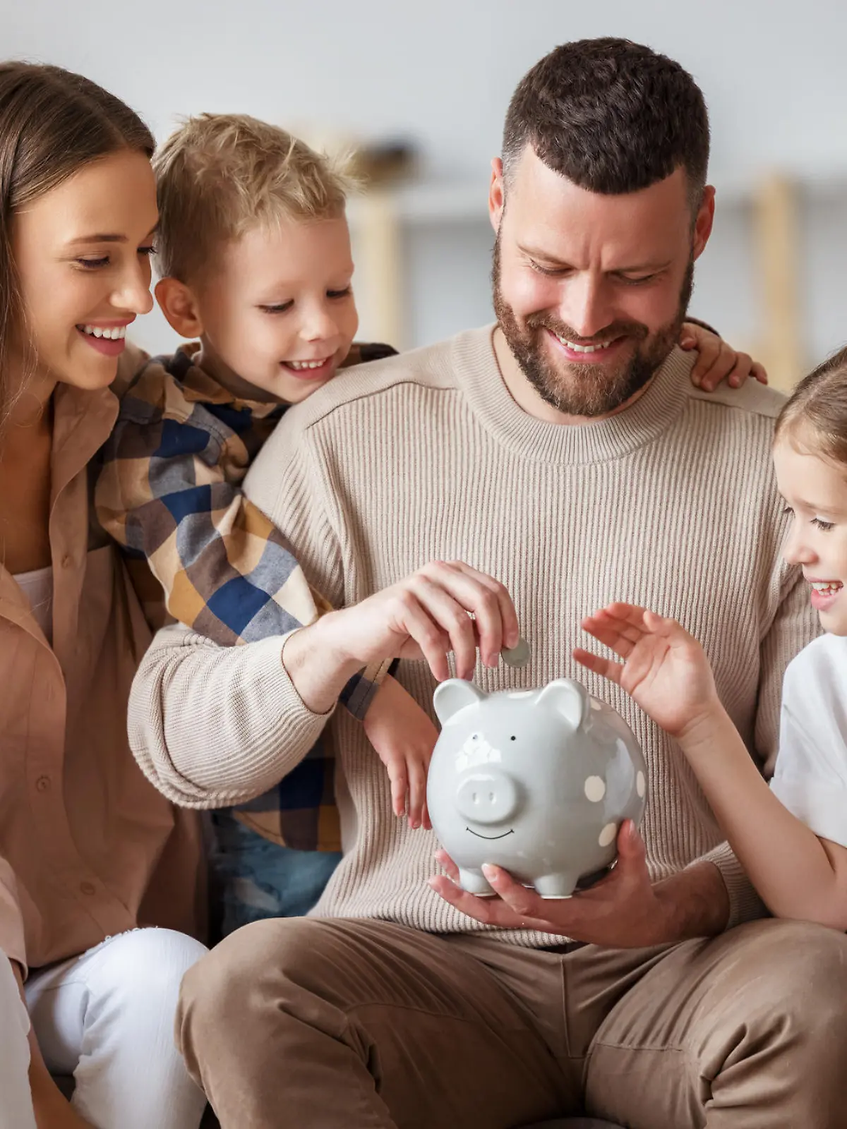 Happy family: cheerful mother and father with kids smiling and putting coins into piggy bank while sitting on sofa at home