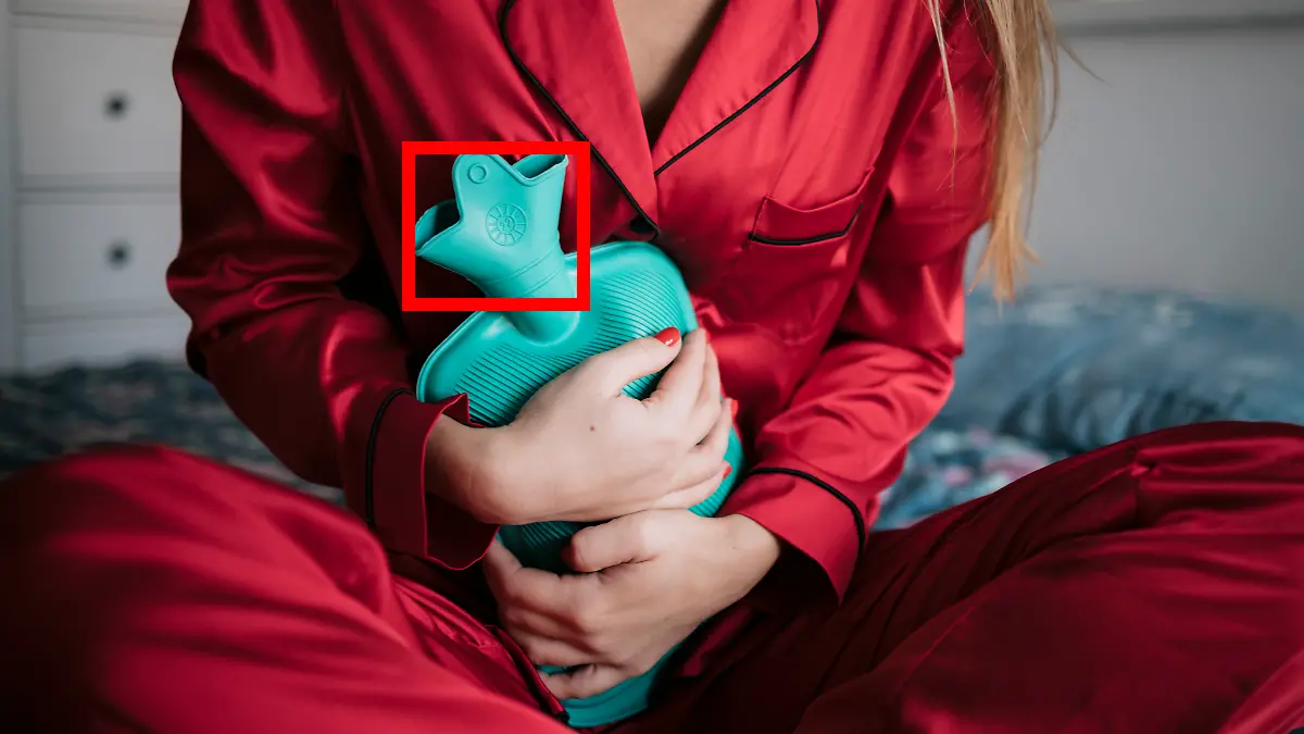 Frau sitzt mit einer Wärmflasche auf dem Bett