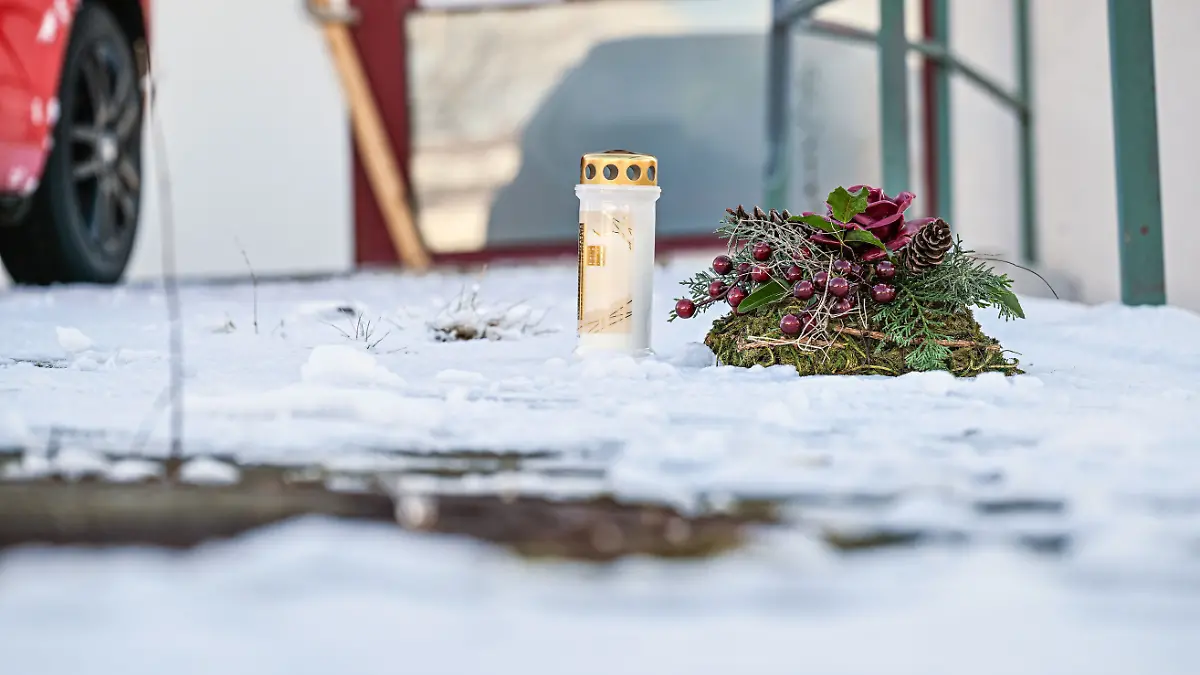 Eine Kerze steht neben einem Kranz an einem Tatort vor einem Firmengelände im Landkreis Reutlingen. 