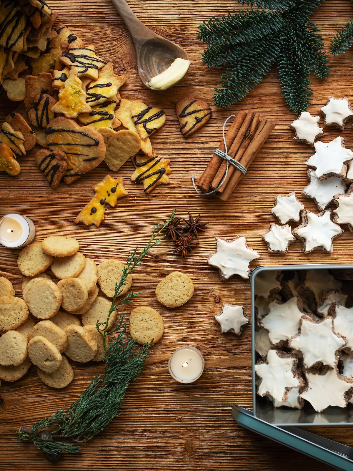 Verschiedene Weihnachtskekse, die verteilt auf einem Holztisch liegen, vereinzelt auch in Keksdosen