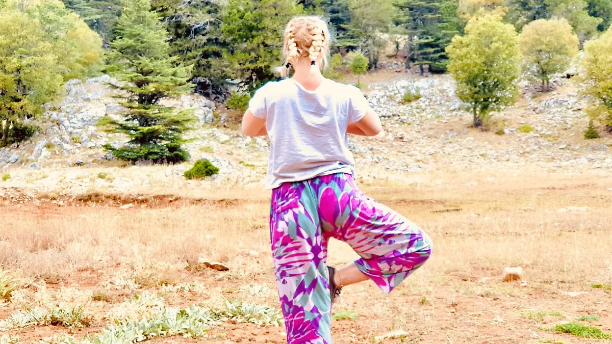 Blonde Frau von hinten macht die Yogaposition "Baum". Im Hintergrund ist ein Wals