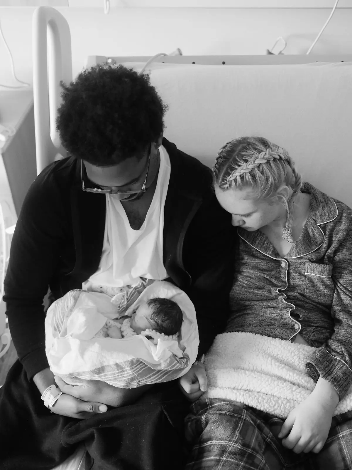 Frau und Mann mit Kind im Arm auf Bett. 