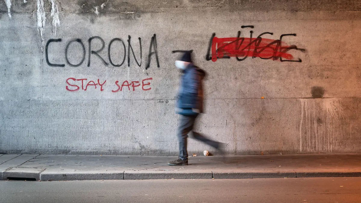 11.01.2021, Hessen, Offenbach: Ein Mann mit Mund-Nasen-Schutz geht durch eine Offenbacher Eisenbahnunterführung, an deren Wand «Corona Lüge» geschrieben steht, wobei mit roter Farbe das gesprühte Wort «Lüge» (r) durchgestrichen wurde. Stattdessen wurde «Stay Safe» (Bleibe sicher) unter das Wort «Corona» gesprüht. Foto: Frank Rumpenhorst/dpa +++ dpa-Bildfunk +++
