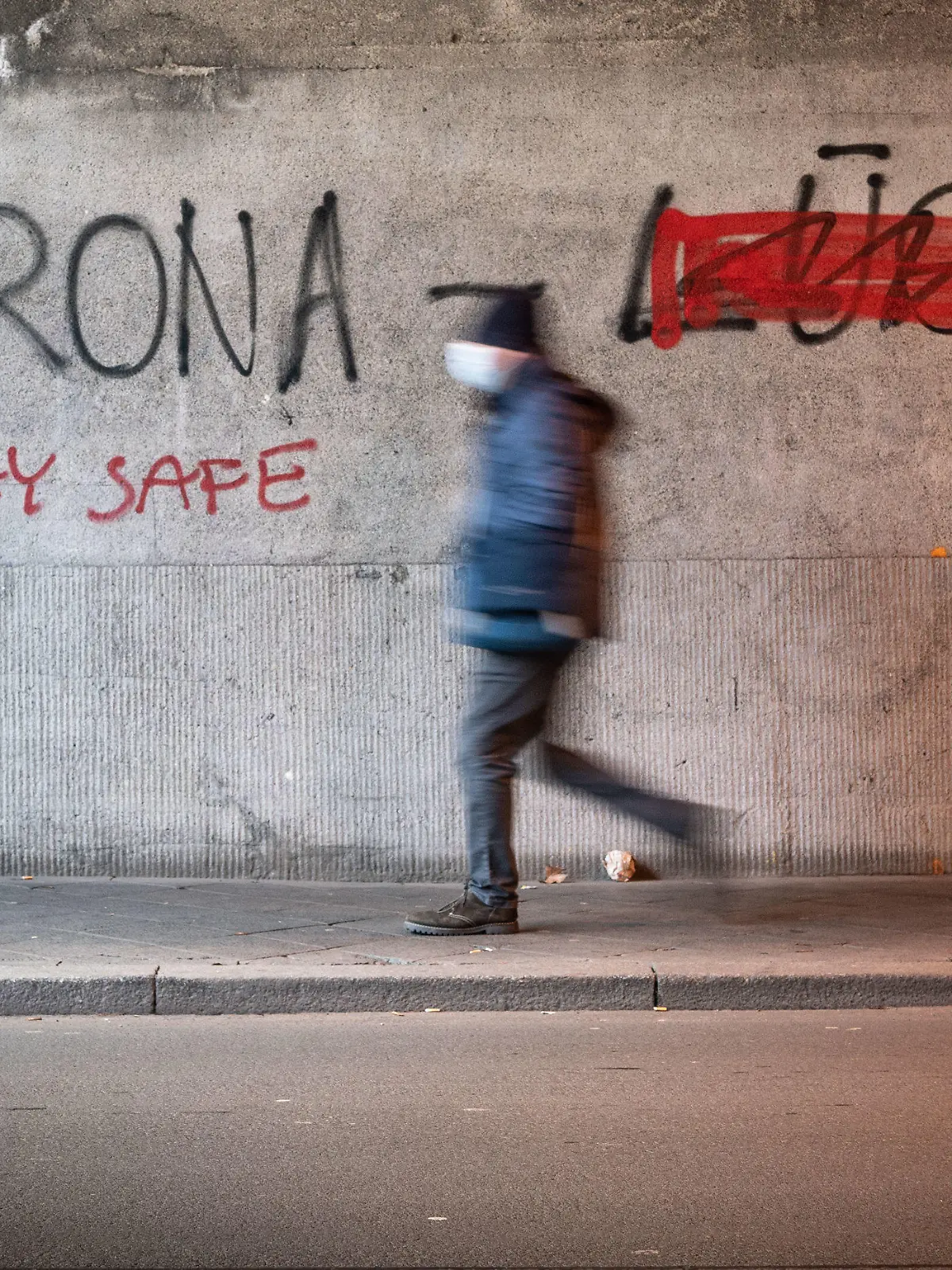 11.01.2021, Hessen, Offenbach: Ein Mann mit Mund-Nasen-Schutz geht durch eine Offenbacher Eisenbahnunterführung, an deren Wand «Corona Lüge» geschrieben steht, wobei mit roter Farbe das gesprühte Wort «Lüge» (r) durchgestrichen wurde. Stattdessen wurde «Stay Safe» (Bleibe sicher) unter das Wort «Corona» gesprüht. Foto: Frank Rumpenhorst/dpa +++ dpa-Bildfunk +++