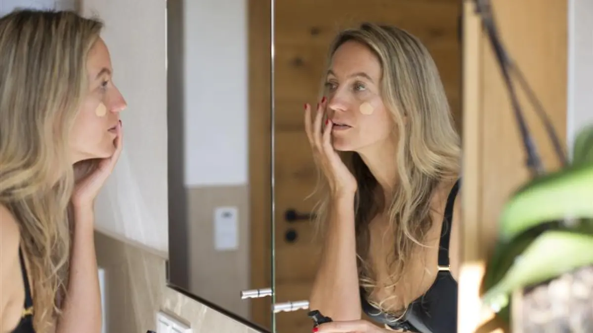 Frau trägt Foundation vor dem Spiegel auf.