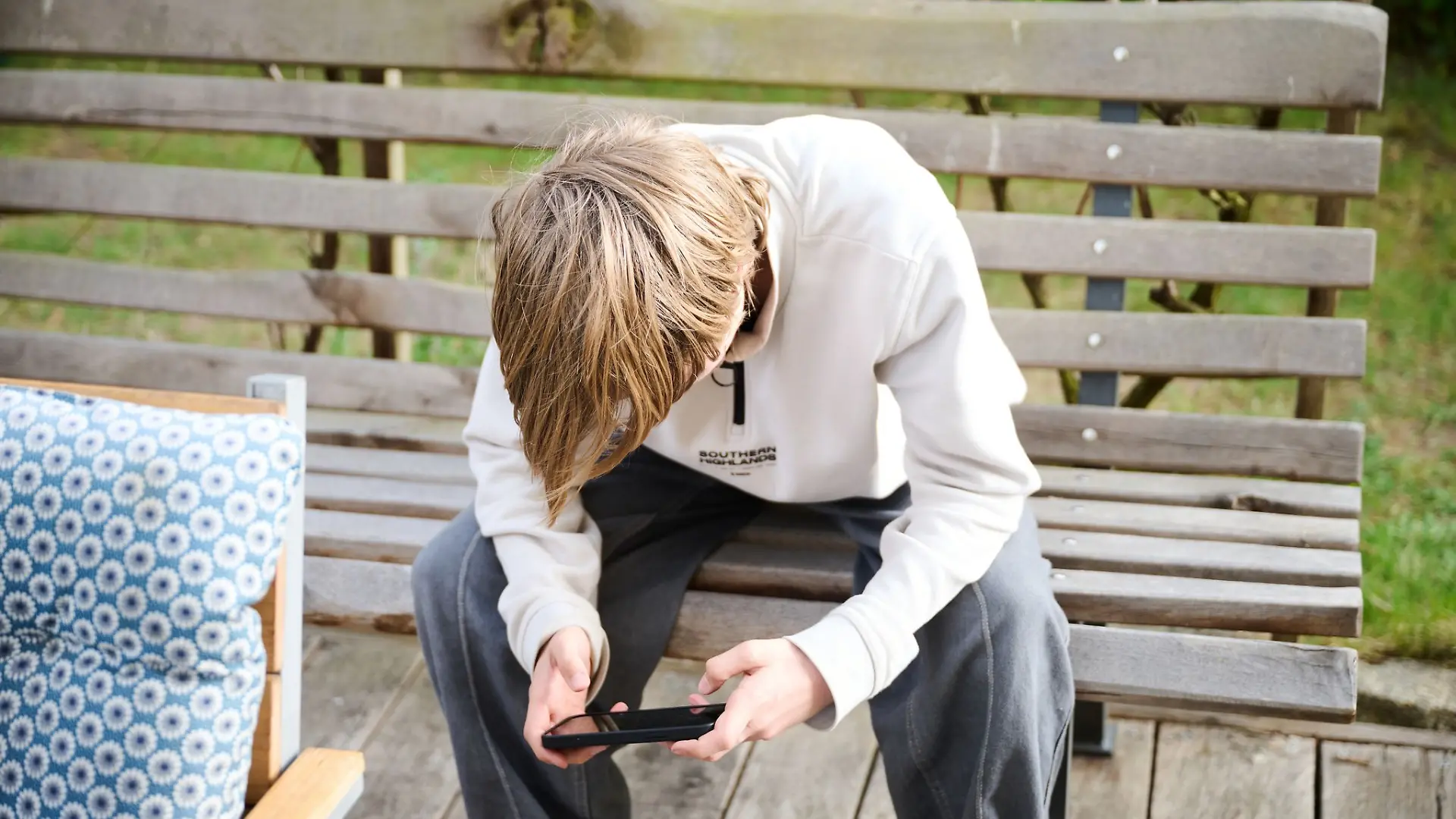 Ein Jugendlicher sitzt auf einer Bank und schaut auf sein Smartphone. (Symbolfoto)