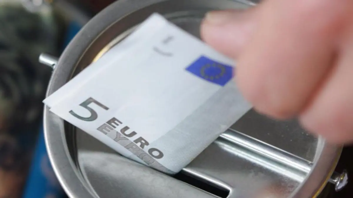 Ein Geldschein wird in eine Spendendose gesteckt