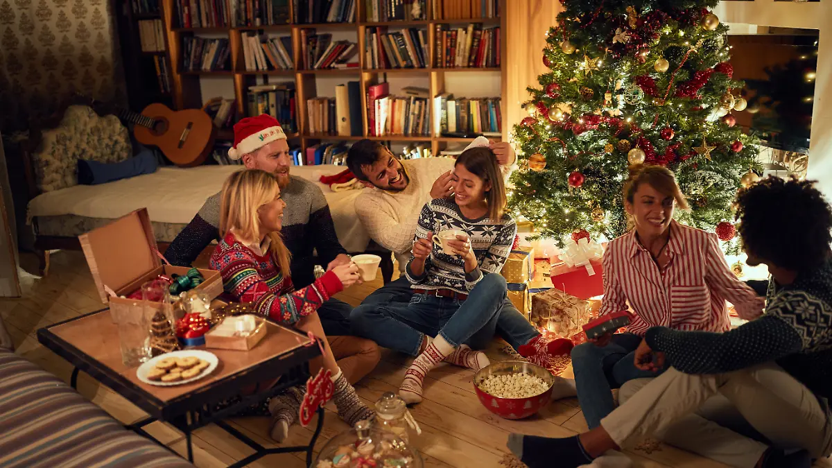 Fröhliche Freunde sitzen neben einem Weihnachtsbaum, essen Weihnachtsplätzchen, trinken Kakao und haben Spaß.