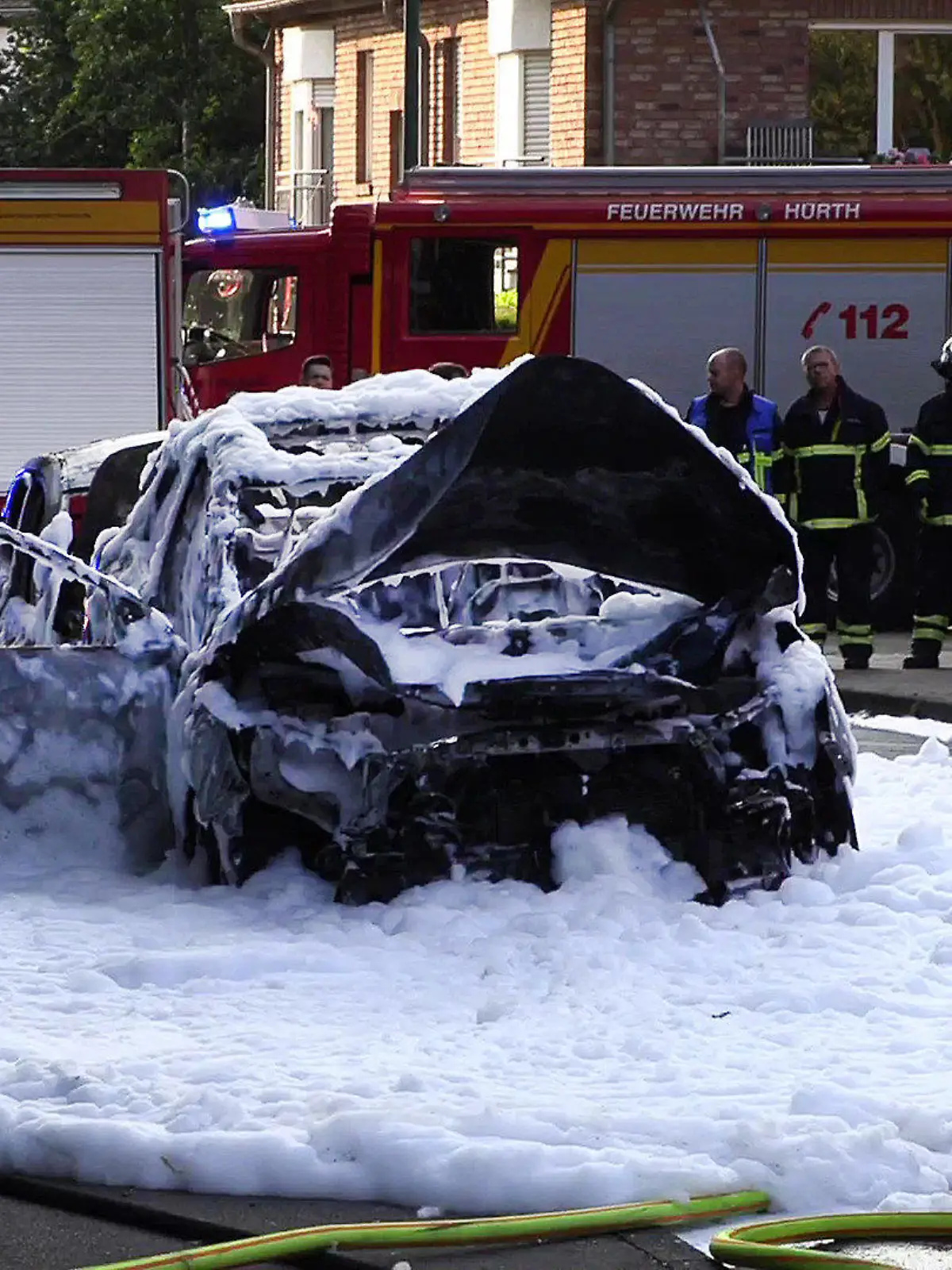 02.08.2021, Nordrhein-Westfalen, Hürth: Vom Löschschaum bedeckt steht ein Auto nach einer Explosion auf der Straße. Nach Polizeiangaben wurden dabei zwei Menschen verletzt, einer davon schwer. In dem Wagen habe es aus noch ungeklärter Ursache eine Detonation gegeben, sagte ein Polizeisprecher am Abend. Foto: TNN/dpa +++ dpa-Bildfunk +++