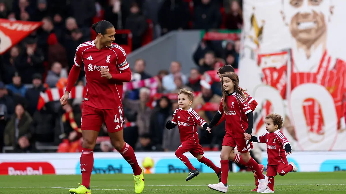 Liverpool-Kapitän Virgil van Dijk (l.) mit den Söhnen (2.v.l. und r.) von Diogo Jota. im  Hintergrund ein Transparent mit einem  Foto des Verstorbenen 