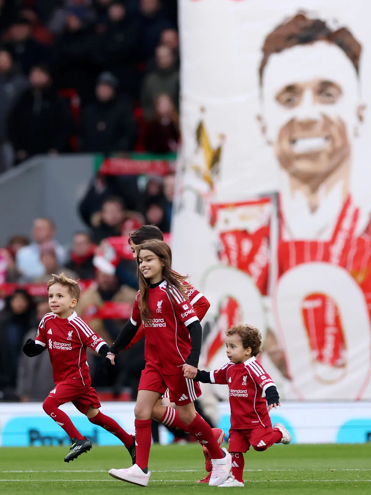 Liverpool-Kapitän Virgil van Dijk (l.) mit den Söhnen (2.v.l. und r.) von Diogo Jota. im Hintergrund ein Transparent mit einem Foto des Verstorbenen