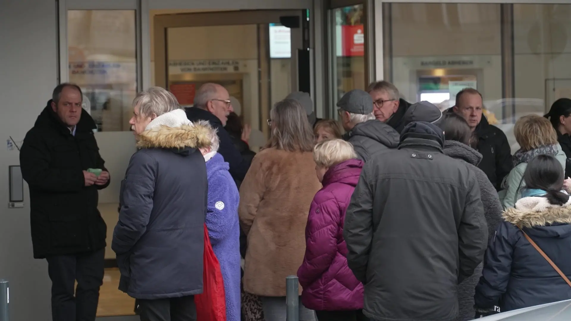 Teils fassungslos stehen Menschen vor der Sparkasse